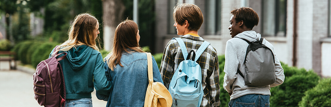 Back view of multiethnic teenagers with backpacks walking together on street